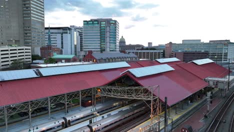 Train-station-with-red-roofs,-trains,-and-surrounding-urban-skyline