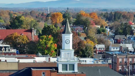 A-white-clock-tower-stands-tall-amid-autumn-colored-trees-in-a-serene-town