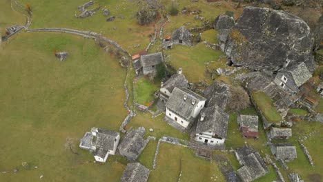 Aerial-drone-bird's-eye-view-flying-high-over-old-stonewalled-village-houses-in-Cavergno,-District-of-Vallemaggia,-Canton-of-Ticino-in-Switzerland-at-daytime