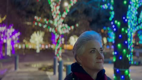 Senior-woman-walking-at-night-in-a-city-decorated-with-glowing-Christmas-lights