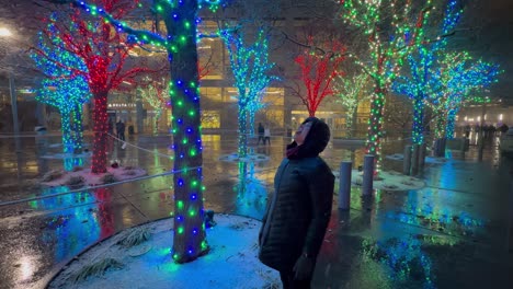 Senior-woman-catching-snow-in-her-mouth-in-a-city-park-with-Christmas-lights