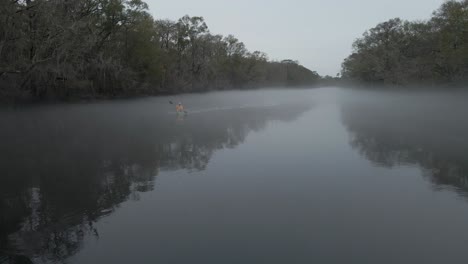 Bearded-man-with-a-yellow-jacked-paddling-a-kayak-out-from-a-thick-fog-that-is-covering-river