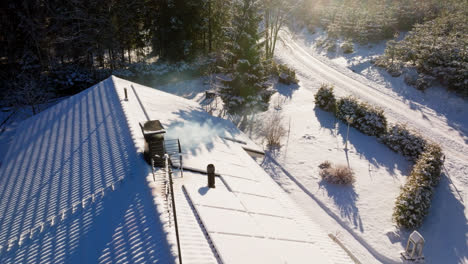 Aerial-view-around-a-smoking-chimney-and-snow-covered-solar-panels,-on-a-house
