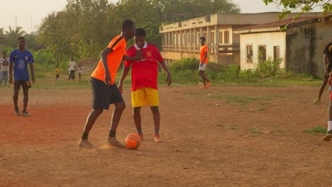 Un-Joven-Empuja-A-Un-Oponente-De-Fútbol-Y-Luego-Patea-El-Balón-Hacia-La-Portería-En-Un-Campo-De-Fútbol-Comunitario-En-Kumasi,-Ghana