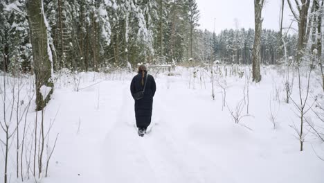 Winter,-deep-snowfall-on-the-ground-as-wrapped-up-young-woman-walks-on