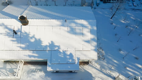 Drone-De-Alto-ángulo-Disparado-Frente-A-Paneles-Fotovoltaicos-Nevados,-Soleado-Día-De-Invierno-En-Una-Casa-Rural