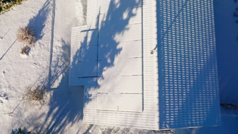 Top-down-drone-shot-over-snow-covered-solar-panels,-on-a-house-roof,-golden-hour