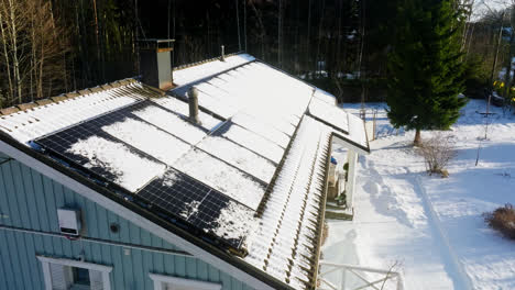 Aerial-pull-back-over-melting-solar-panels-on-a-snowy-house-roof,-winter-day