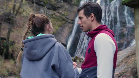 Loving-couple-holding-hands,-talking-while-enjoying-waterfall-scenery,-medium