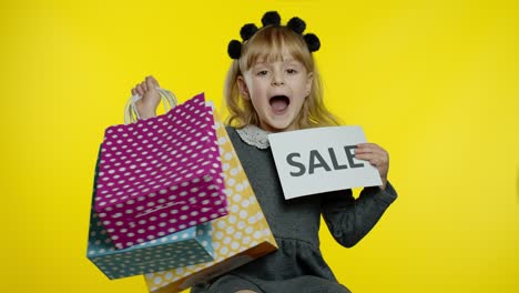 Kleines-Mädchen-Mit-Einkaufstüten-Zeigt-Verkaufswort-Inschrift,-Lächelt-Und-Freut-Sich-über-Gute-Rabatte
