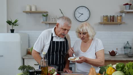 Senior-couple-in-kitchen.-Grandmother-feeding-grandfather-with-raw-sprouts-buckwheat-with-nuts