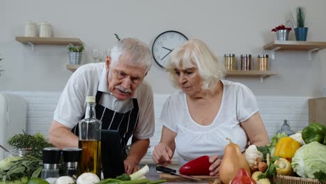 Pareja-Vegana-De-Ancianos-Cocinando-Ensalada-Con-Verduras-Crudas.-Buscando-En-Una-Tableta-Digital-Una-Receta-En-Línea