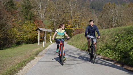 Young-man-and-girl-enjoying-cycle-ride-in-nature-on-sunny-autumn-day,-front-view