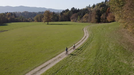 Bike-ride-of-two-cyclists-with-mountain-view,-forests,-and-meadows,-aerial-shot