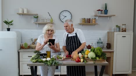 Vegan-senior-grandparents-looking-for-a-culinary-recipe-online-on-digital-tablet,-cooking-salad
