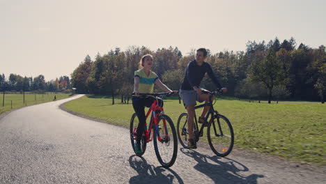 Young-man-and-a-girl-enjoying-cycling-in-nature-on-a-sunny-autumn-day,-tracking