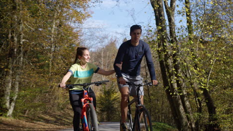Smiling-couple-having-fun-cycling-uphill-through-the-autumn-forest,-front-view