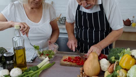 Senior-vegan-grandmother-and-grandfather-cooking-salad-with-fresh-vegetables-in-kitchen-at-home