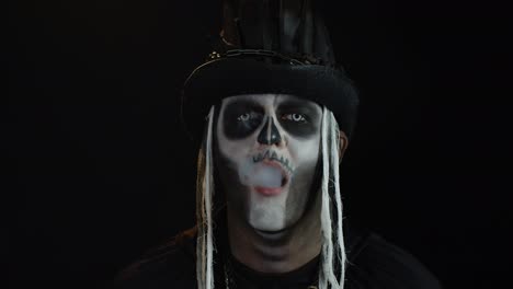 Finsterer-Mann-Mit-Halloween-Skelett-Make-up,-Der-Zigarettenrauch-Aus-Seinem-Mund-Ausatmet-Und-Lächelt