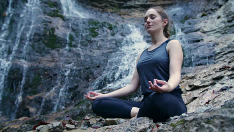 Girl-practicing-yoga-while-waterfall-burbling-in-the-background,-low-angle-shot