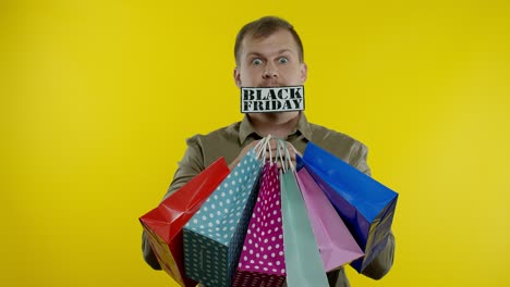 Überraschter-Mann-Zeigt-Einkaufstüten-Und-Die-Aufschrift-„Black-Friday“-Im-Mund.-Gelber-Hintergrund