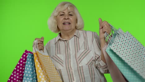 Senior-grandma-raising-shopping-bags,-celebrating,-satisfied-with-purchase,-discount.-Chroma-key
