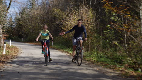 Couple-cycling-on-a-forest-trail,-holding-hands-and-having-fun,-front-view