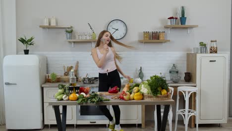 Lovely-vegan-girl-with-long-hair-dancing-and-singing-in-modern-kitchen.-Raw-vegetable-food-diet