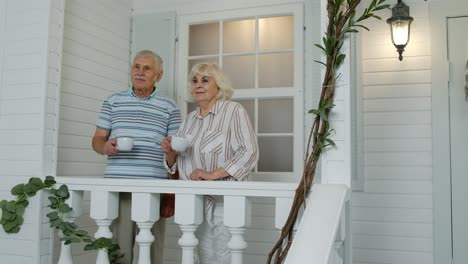 Senior-elderly-Caucasian-couple-drinking-coffee,-looking-ahead-in-porch-at-home.-Mature-family