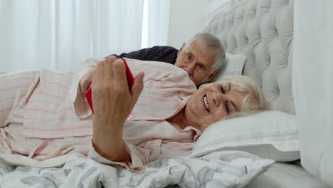 Senior-grandparents-couple-lying-in-bed.-Woman-getting-nervous-about-man-spying-into-mobile-phone