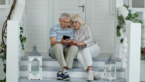 Älteres-Kaukasisches-Paar-Nutzt-Digitales-Tablet-Auf-Der-Veranda-Zu-Hause.-Viel-Spaß-Beim-Online-Shopping,-Neuigkeiten
