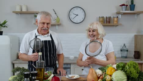 Happy-senior-couple-dancing-while-cooking-together-in-kitchen-with-fresh-vegetables-and-fruits