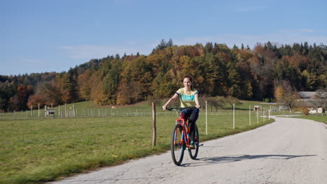 Girl-riding-a-bike-along-the-countryside-road-on-a-sunny-autumn-day,-handheld