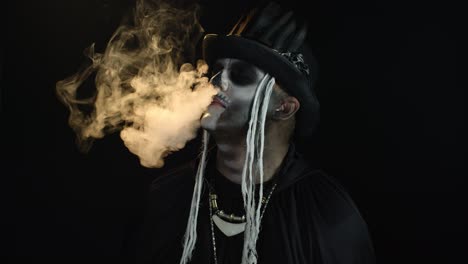 Sinister-man-with-professional-skull-makeup-exhaling-cigarette-smoke-from-his-mouth-and-nose