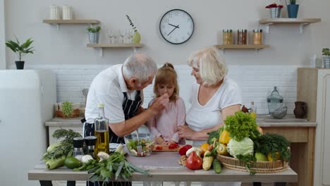 Ältere-Großeltern-In-Der-Küche-Füttern-Enkelkind-Mit-Gehackter-Roter-Paprika.-Vegetarische-Diät
