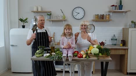 Fröhliches-Veganes-Seniorenpaar-Tanzt-Mit-Enkelin,-Während-Es-In-Der-Küche-Gemüse-Kocht