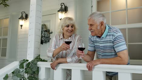 Ein-älteres-Kaukasisches-Paar-Trinkt-Wein,-Blickt-Nach-Vorne-Und-Küsst-Sich-Zu-Hause-Auf-Der-Veranda
