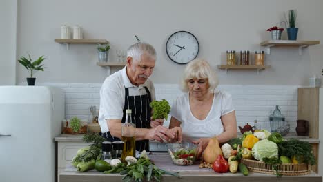 Senior-grandparents-in-kitchen.-Funny-grandpa-joking-on-grandma.-Putting-a-lettuce-about-her-head
