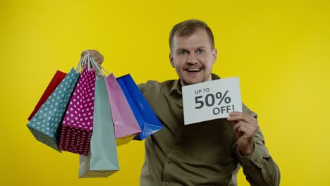 Man-showing-Up-To-50-percent-Off-inscription-and-shopping-bags,-rejoicing-discounts.-Black-Friday