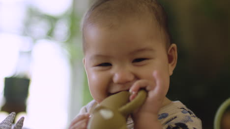 Cute-mixed-race-Asian-baby-chewing-teething-toy-and-smiling-laughing