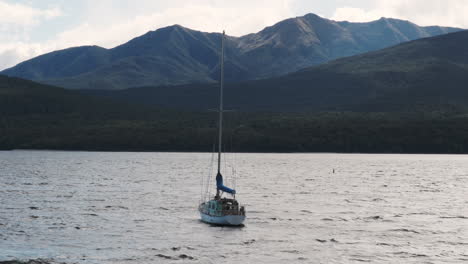 A-sailboat-gently-sways,-set-against-the-breathtaking-backdrop-of-majestic-mountains