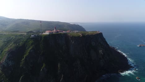 Drone-flying-over-high-hill-rocks-top-view-Atlantic-ocean-shores-around-cape-Cabo-da-Roca-in-Sintra-Portugal-lighthouse-westernmost-point-of-Eurasian-continent-beautiful-archipelagos-natural-scenery