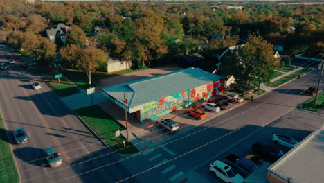 Aerial-drone-pull-away-from-corner-drugstore-"Greetings-from-Georgetown"-mural-in-Austin-suburb-Georgetown,-Texas