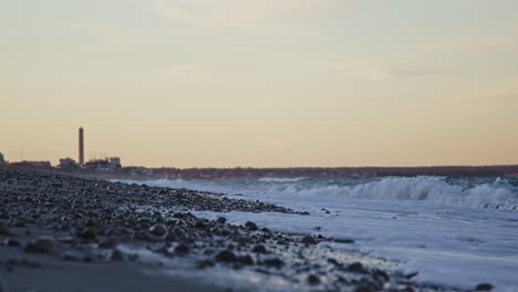 Wide-shot-of-waves-crashing-on-a-beach-during-golden-hour-with-power-station-in-background