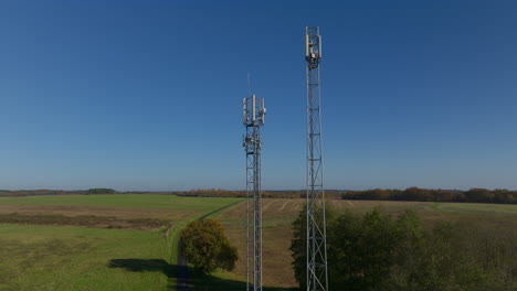 Two-cellular-towers-in-the-middle-of-farmland-during-sunrise,-aerial-dolly-up-tilting