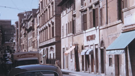 Calle-Estrecha-En-El-Centro-Rodeada-De-Tiendas-En-Roma-En-Los-Años-1960