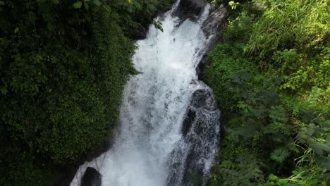 Looking-down-on-a-powerful-waterfall-surrounded-by-jungle-in-the-North-of-Bali-in-the-summer,-aerial