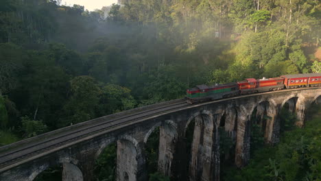 Pullback-Aerial-Drone-Shot-of-Diesel-Train-Crossing-9-Arches-Bridge-on-Misty-Morning-Night-Train