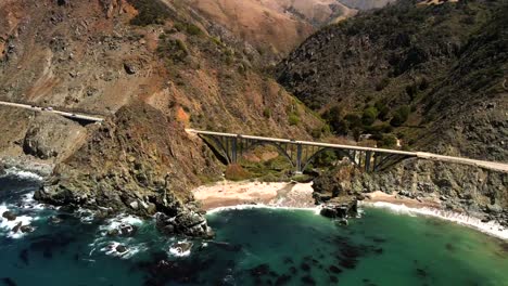 Capture-a-cinematic-and-panoramic-aerial-perspective-of-Big-Sur,-with-a-focus-on-showcasing-the-Bixby-Creek-Bridge-and-the-scenic-highway