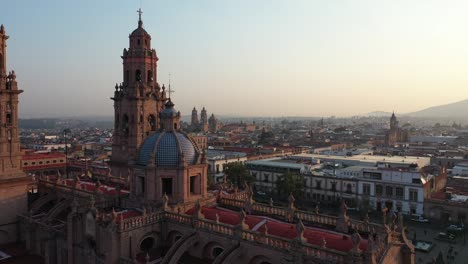 Drone-flies-over-the-majestic-Morelia-Cathedral-at-dawn,-the-warm-sunlight-bathing-its-historic-facade